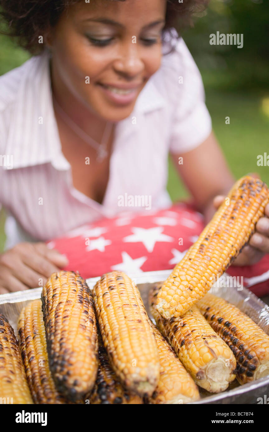 Woman taking grilled corn on the cob out of aluminium dish - Stock Photo