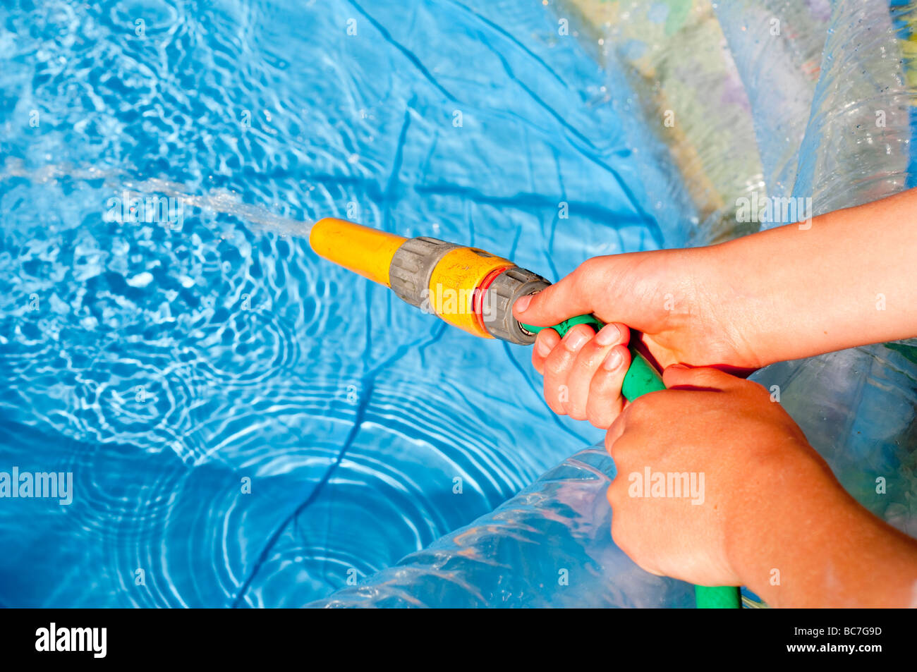 A close up of a child filling a paddling pool with water Stock Photo