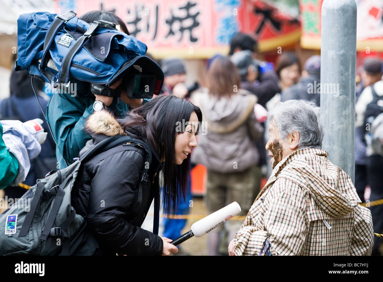 A Japanese TV crew interviewing an old lady with mud on her face Stock Photo