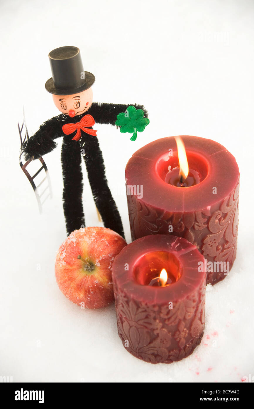 Chimney sweep, apple and red candles in snow - Stock Photo