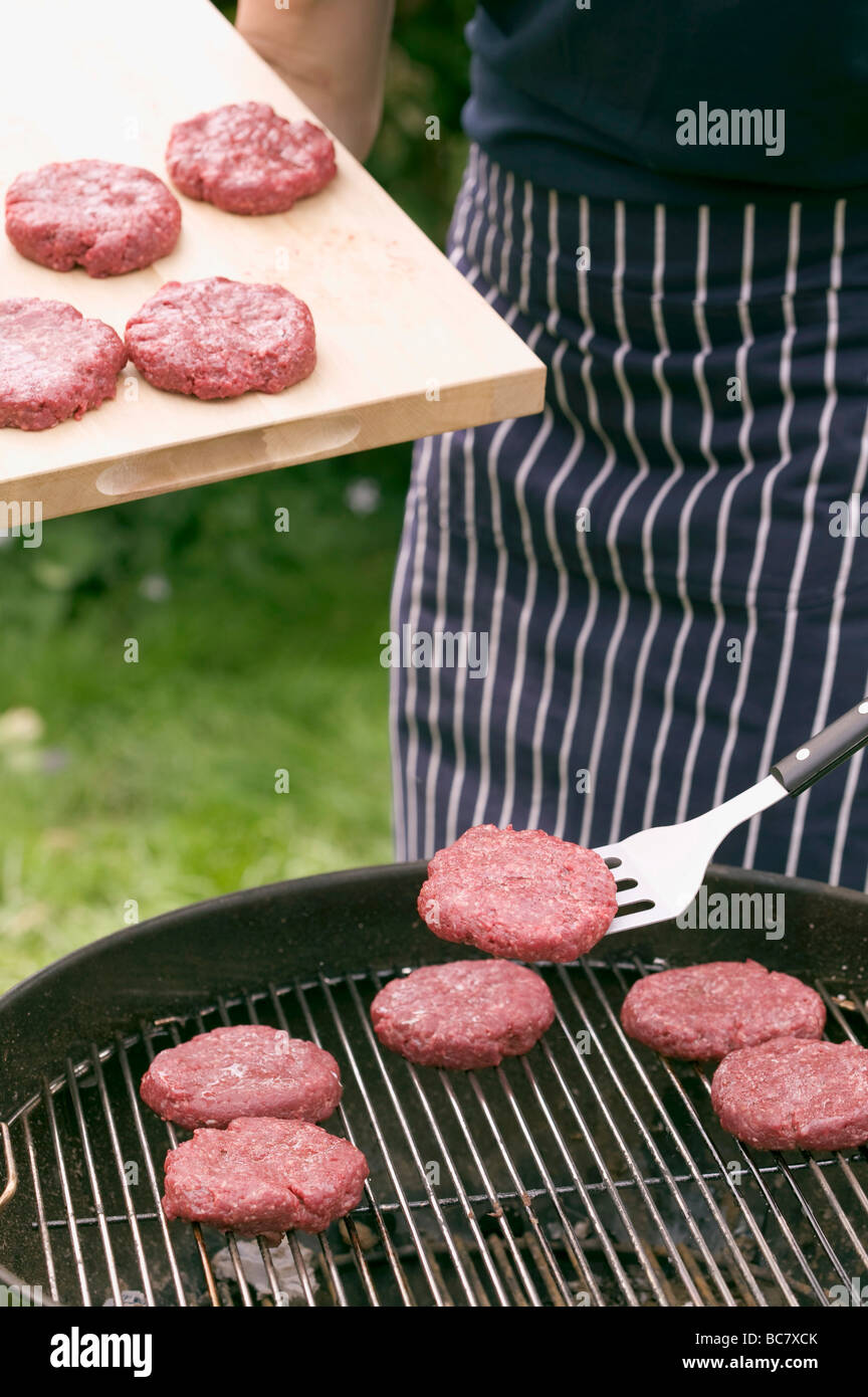 Man placing raw burgers on barbecue grill rack Stock Photo - Alamy