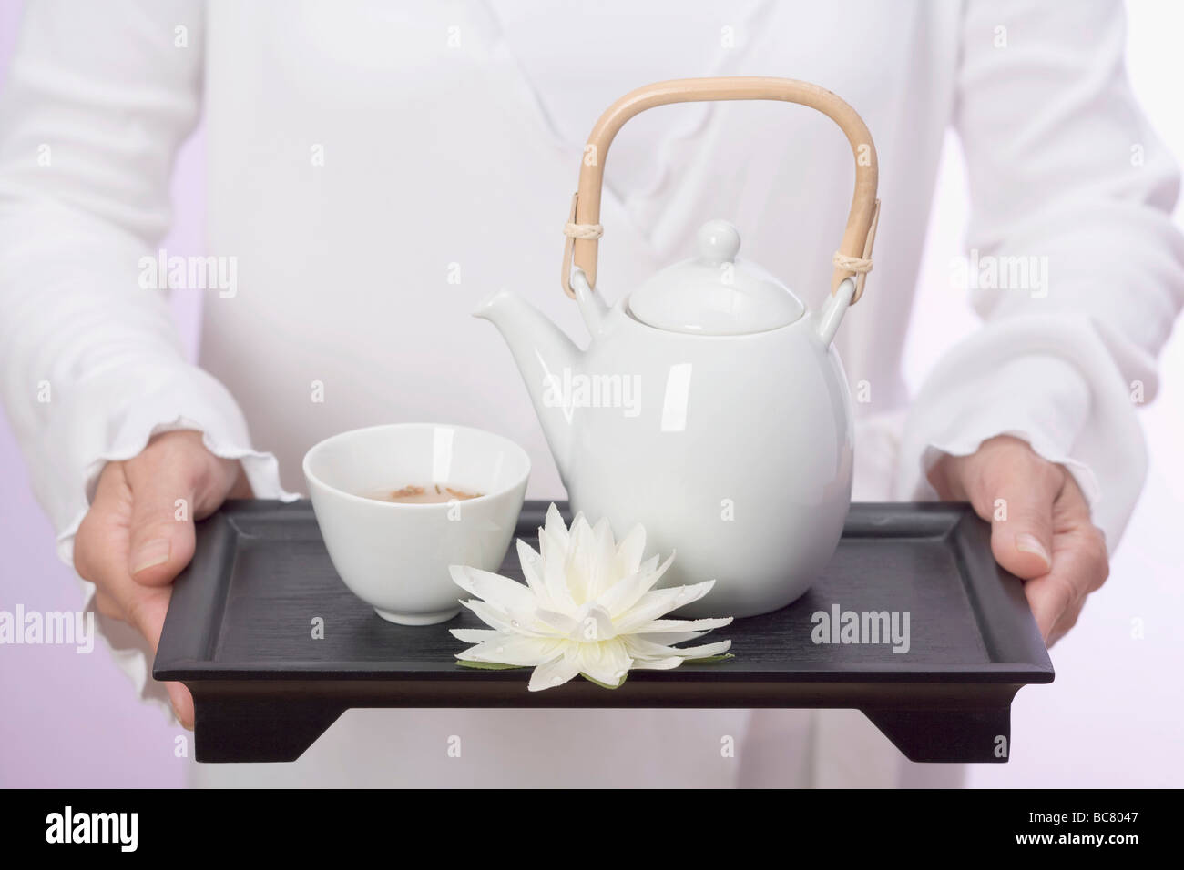 Woman holding teapot, tea bowl and water lily on tray - Stock Photo