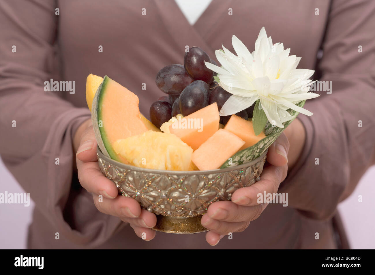 Woman holding bowl of fresh fruit with water lily - Stock Photo