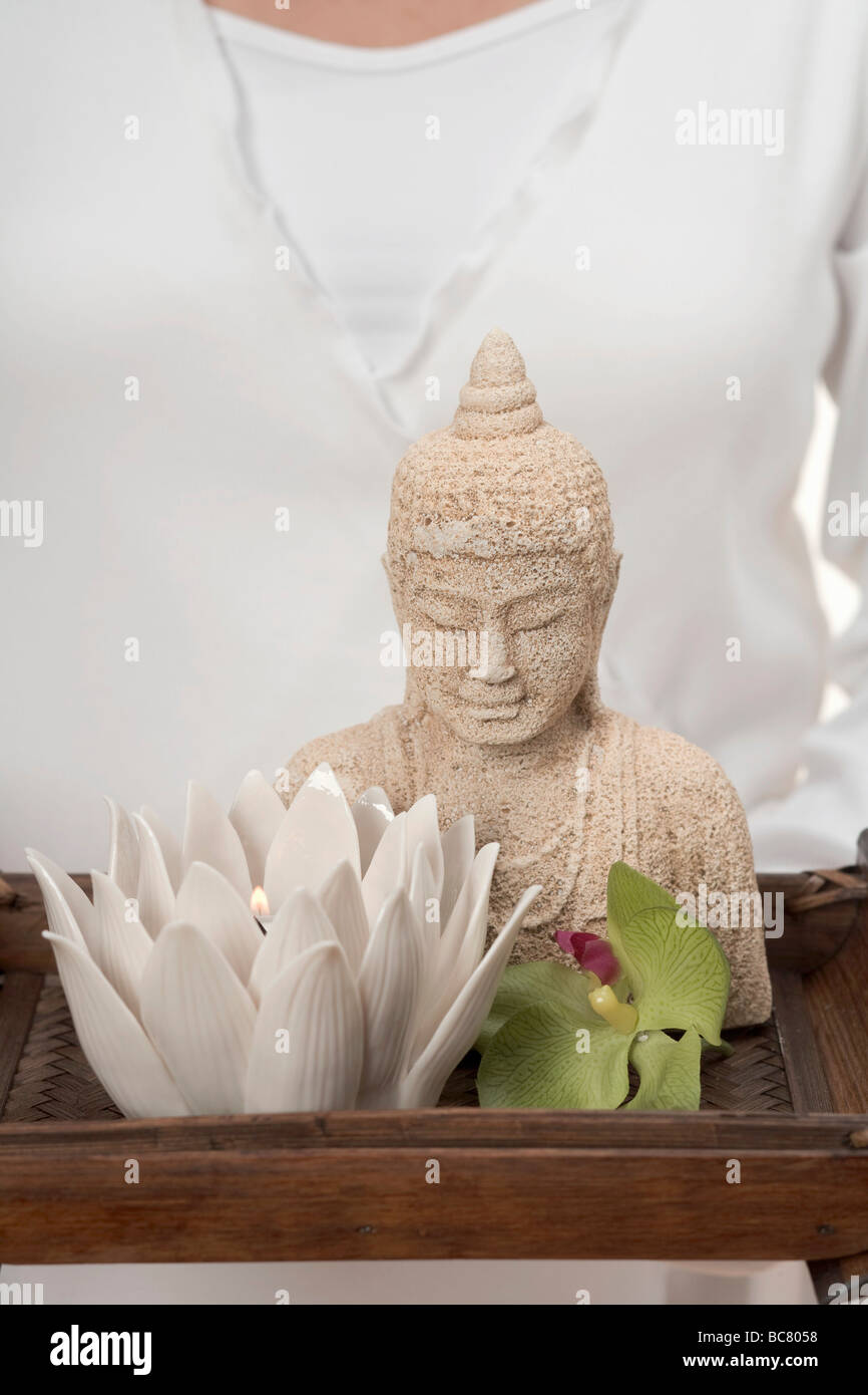 Woman holding statue of Buddha, candle and orchid on tray - Stock Photo