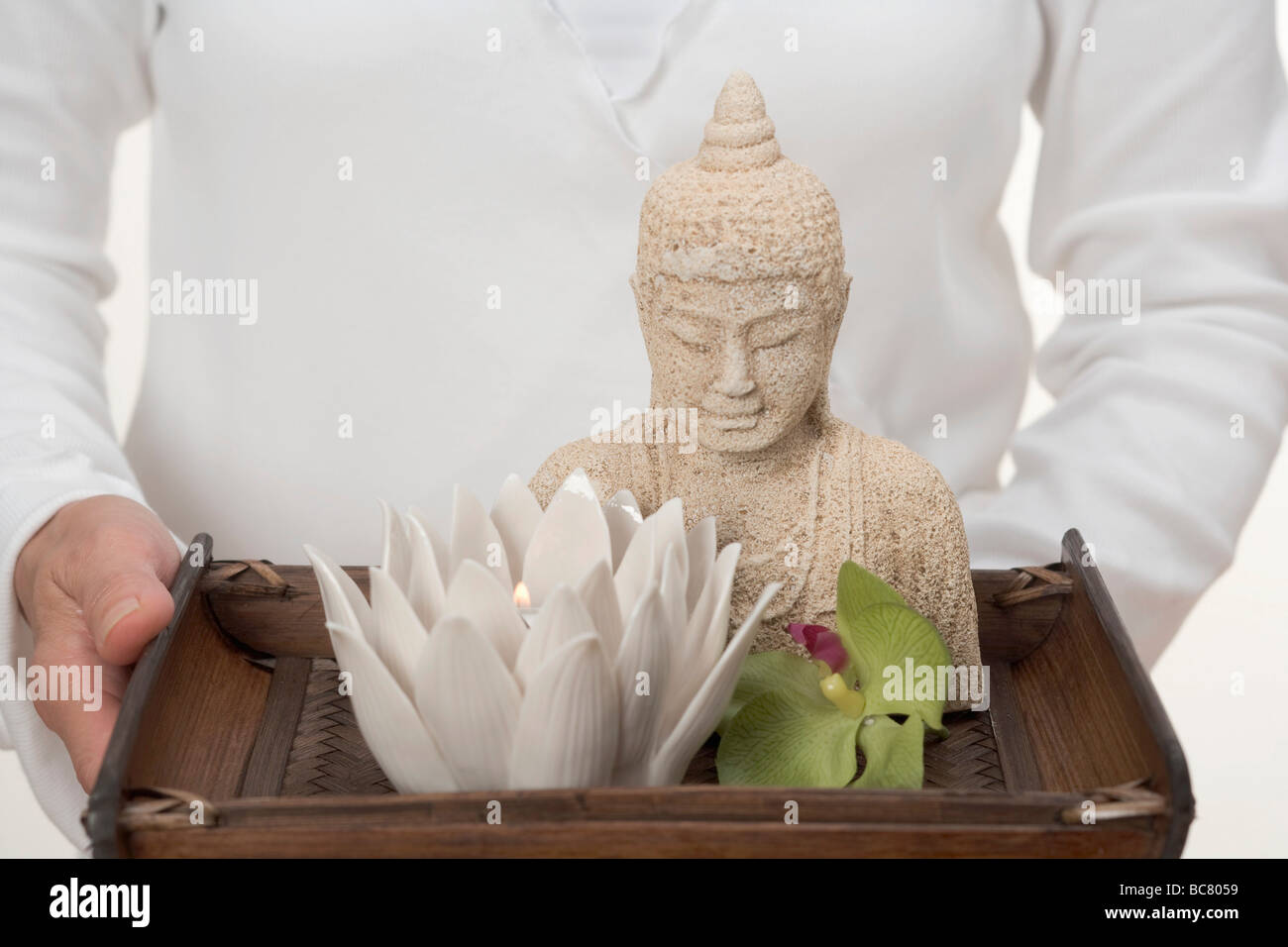 Woman holding Buddha statue, candle and orchid on tray - Stock Photo