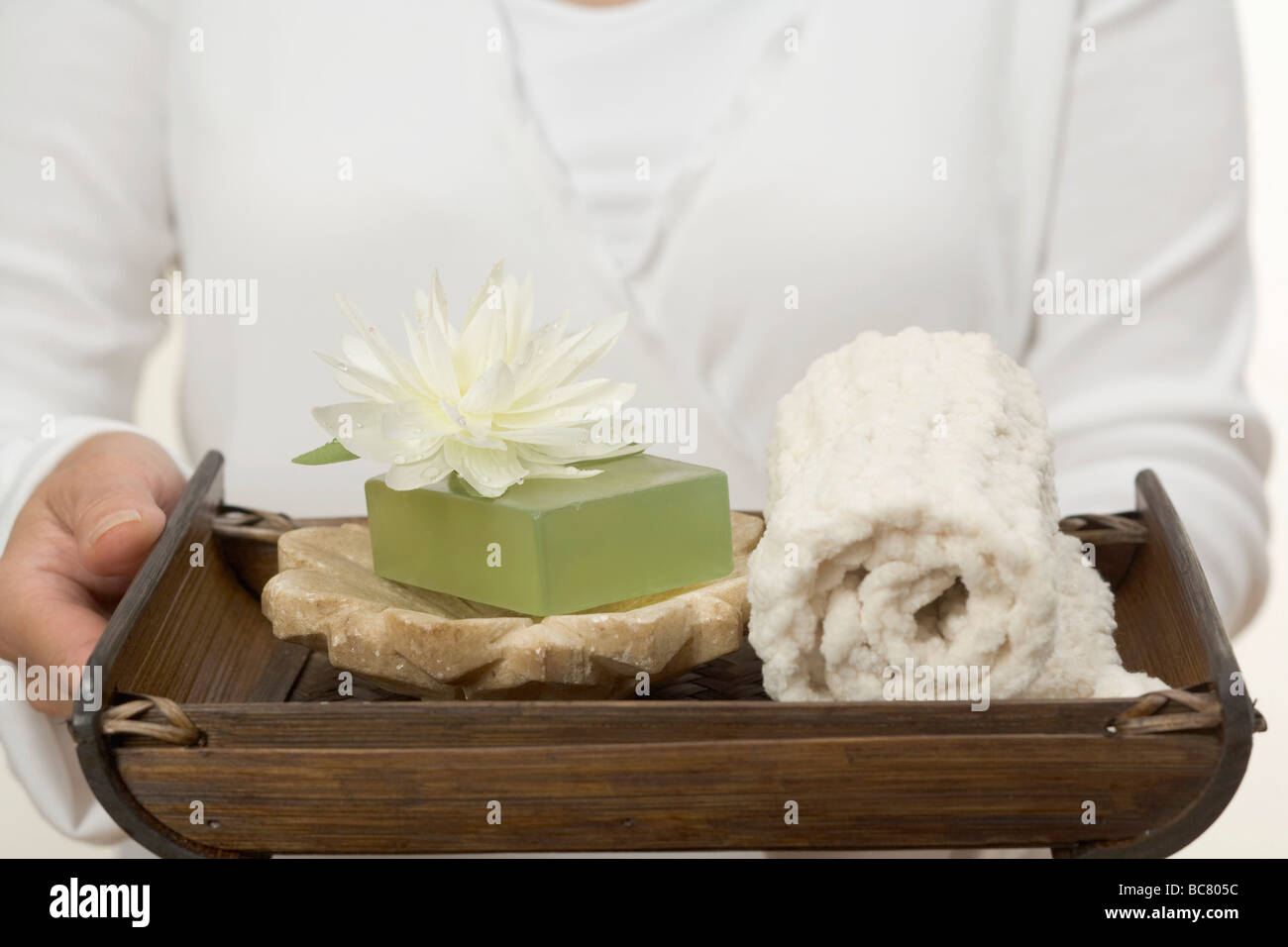 Woman holding soap, water lily and towel on tray - Stock Photo