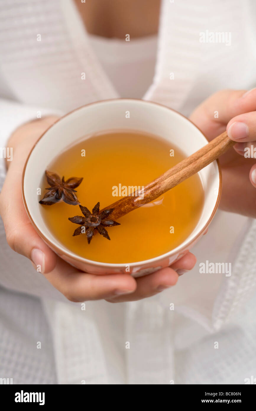 Woman holding bowl of tea with star anise & cinnamon stick - Stock Photo