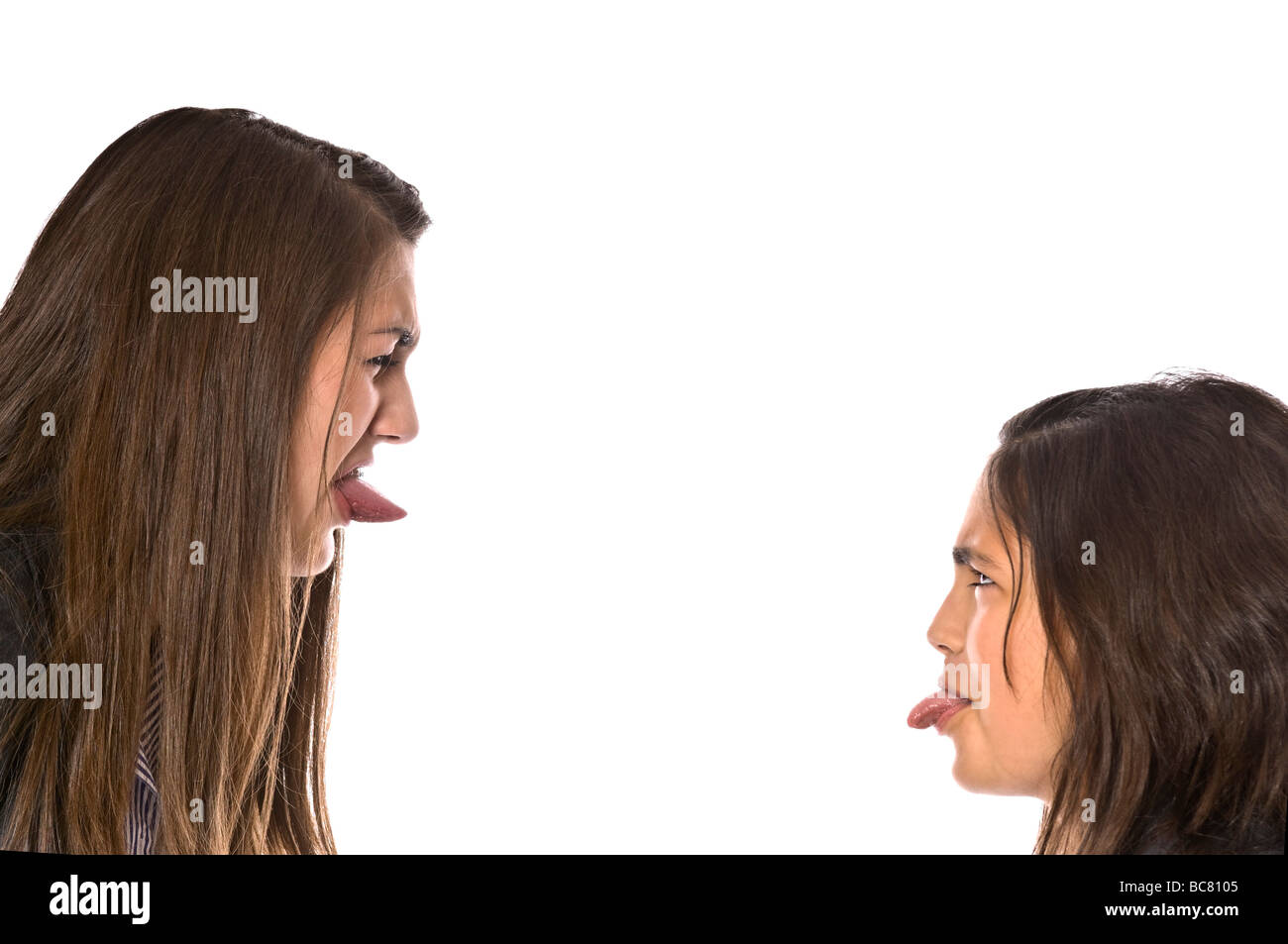 Horizontal close up portrait of angry teenage school girls poking their tongues out during a fight against a white background Stock Photo