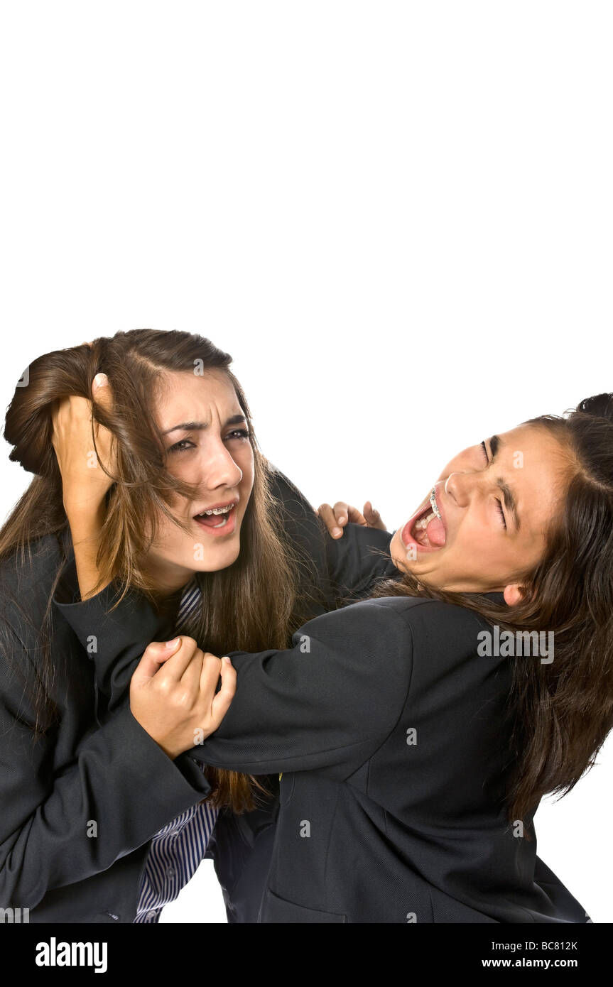 Vertical close up portrait of angry teenage school girls pulling each others hair during a fight against a white background Stock Photo