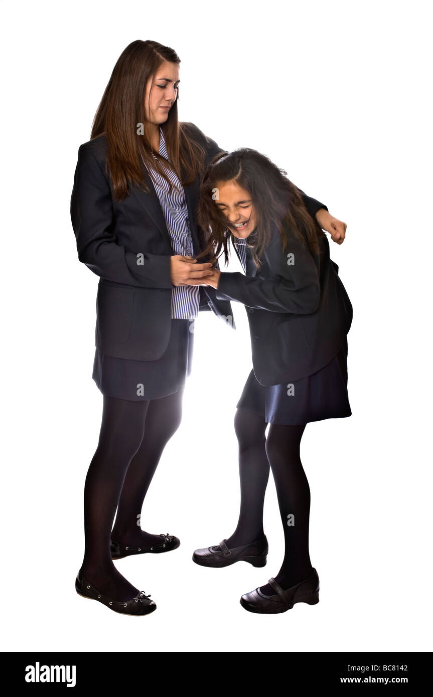 Vertical full length portrait of a teenage school girl bullying a younger girl against a white background Stock Photo