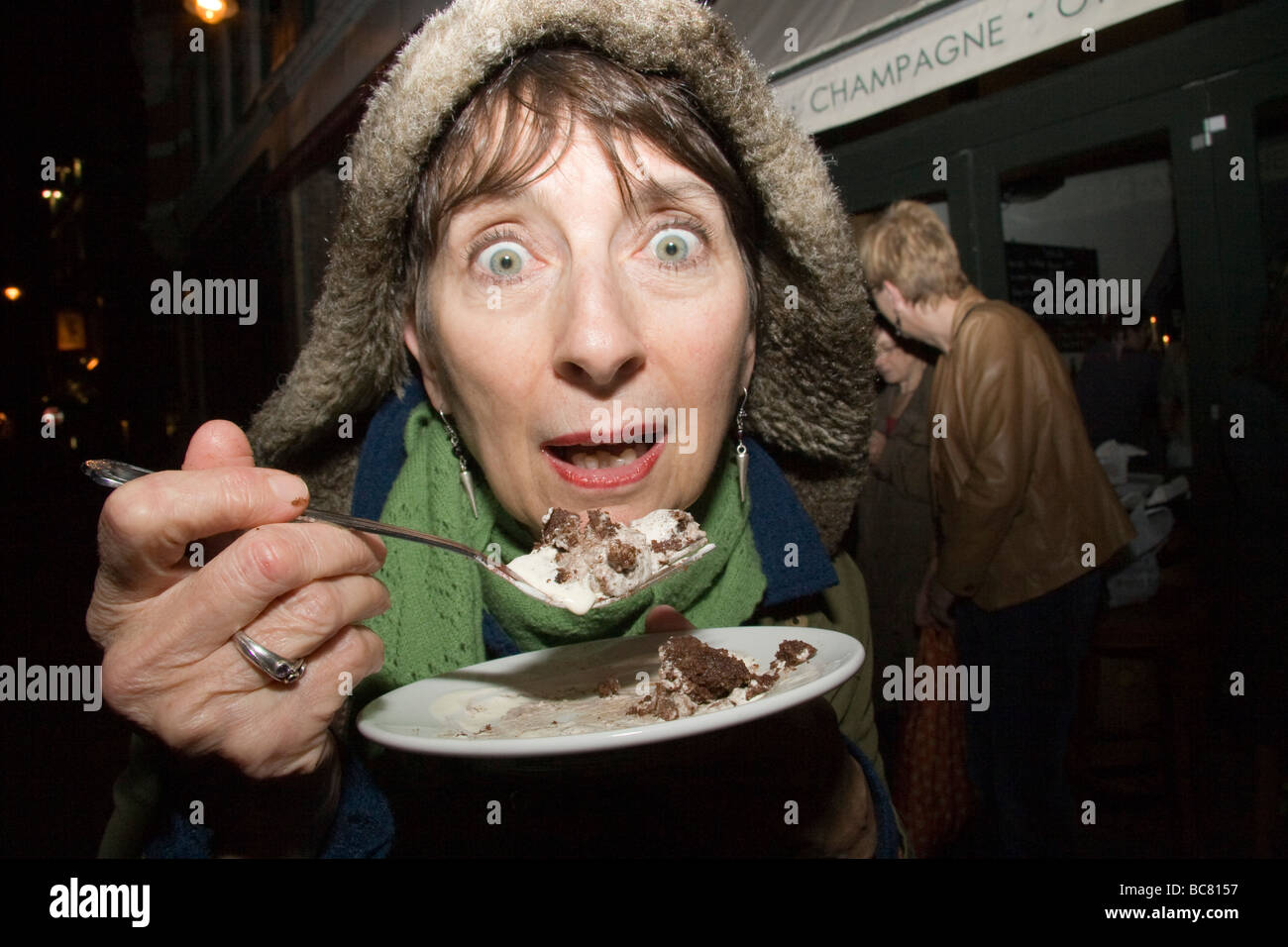 Woman in hooded coat eats cake with a fork while looking at the camera Stock Photo
