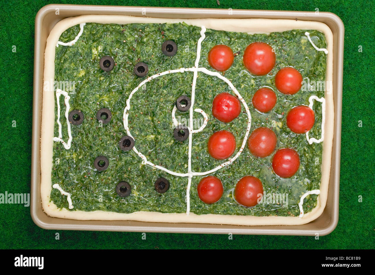 Spinach pizza with tomatoes & olives depicting a football pitch - Stock Photo