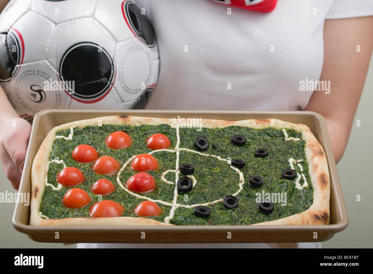 Female footballer holding spinach pizza with tomatoes & olives - Stock Photo