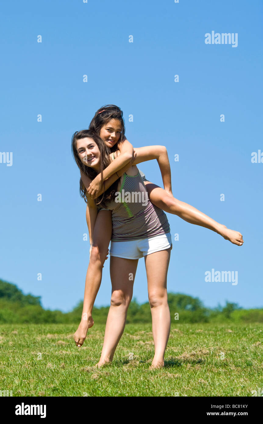 Vertical portrait of two sisters outside having a piggy back ride on a bright sunny day Stock Photo