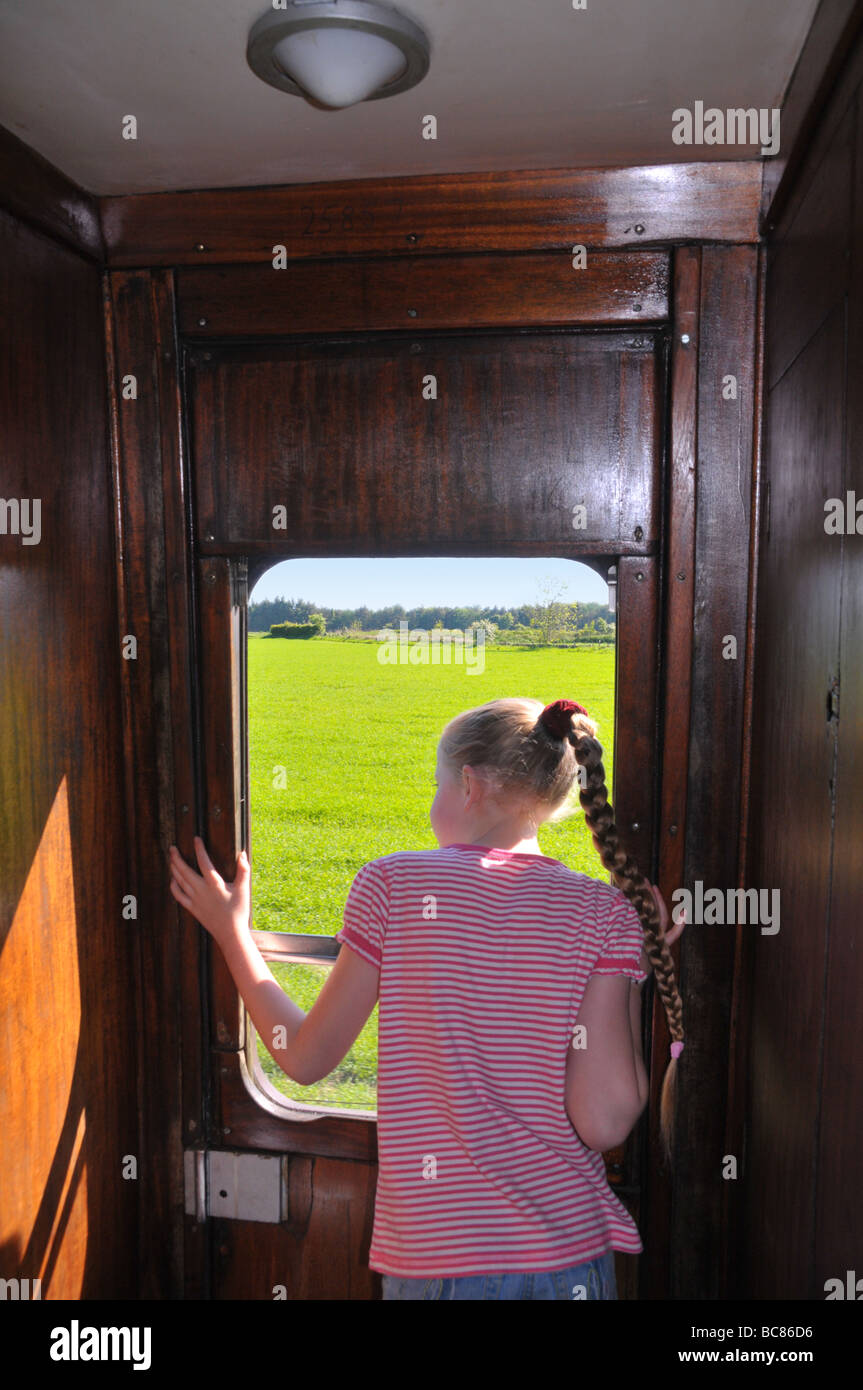 A young girl looks out the window of an old moving train. Stock Photo