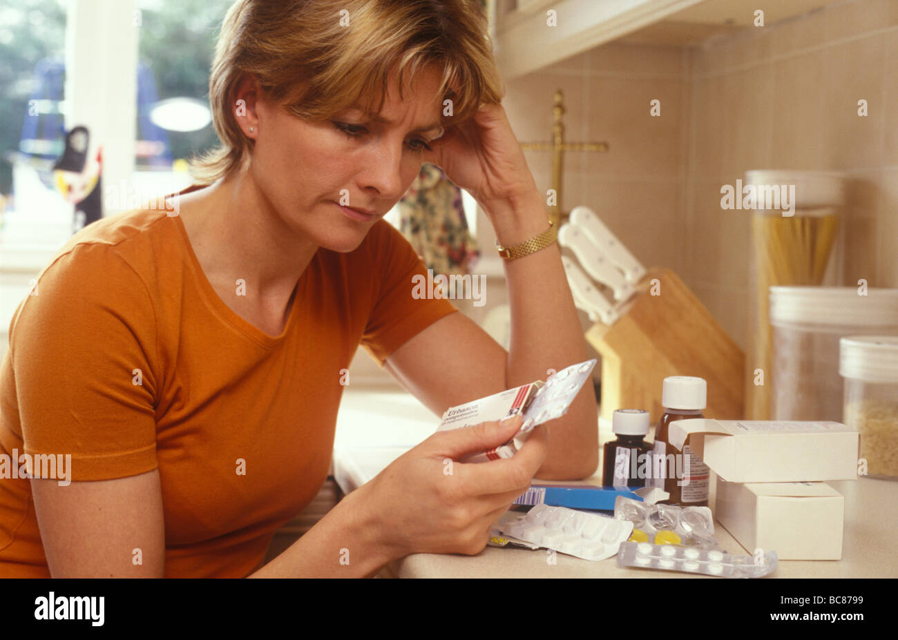 woman in her kitchen with a mixture of drugs deciding what to take Stock Photo