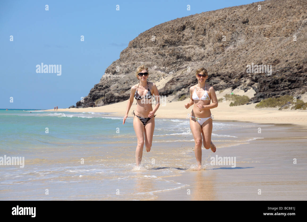 Two young women running on the beach, Fuerteventura, Spain Stock Photo