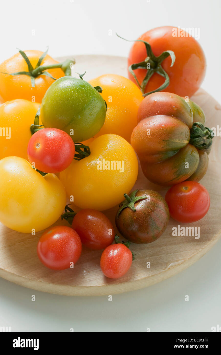 Various types of tomatoes on wooden plate - Stock Photo