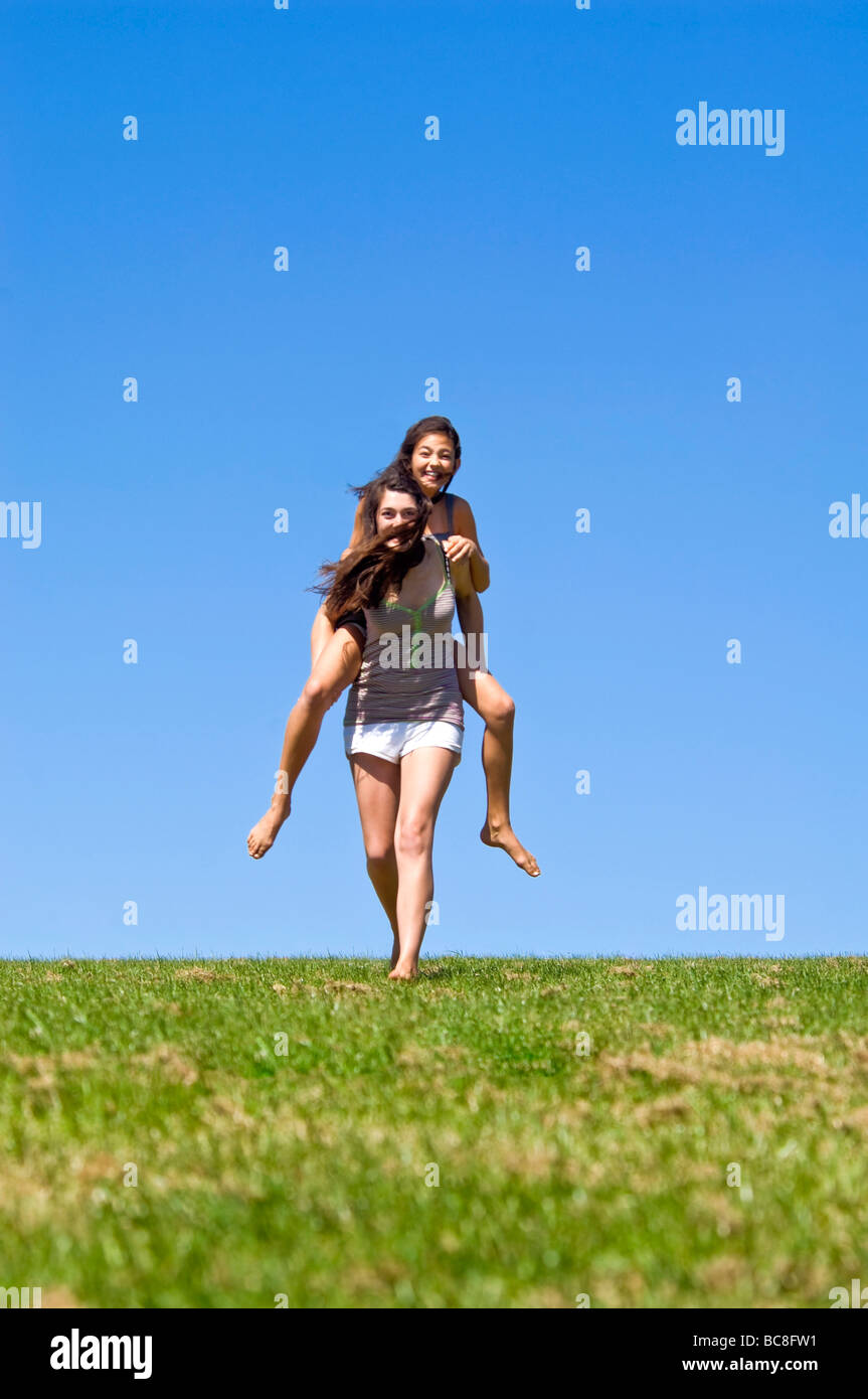 Vertical portrait of two young sisters having great fun having piggy back rides on a bright sunny day Stock Photo