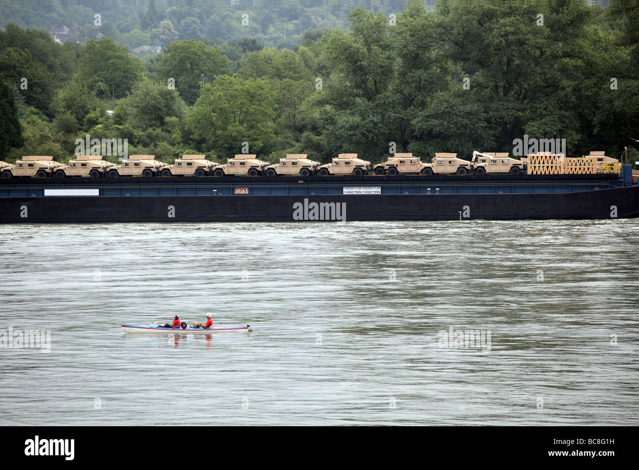 Humvee Vehicles on transport along the River Rhine watched in amazement by two people in a kayak Germany Europe Stock Photo