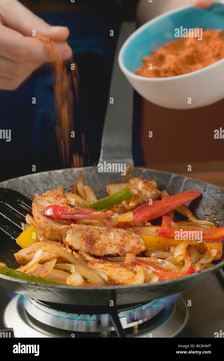 Adding chilli powder to chicken with onions and peppers - Stock Photo
