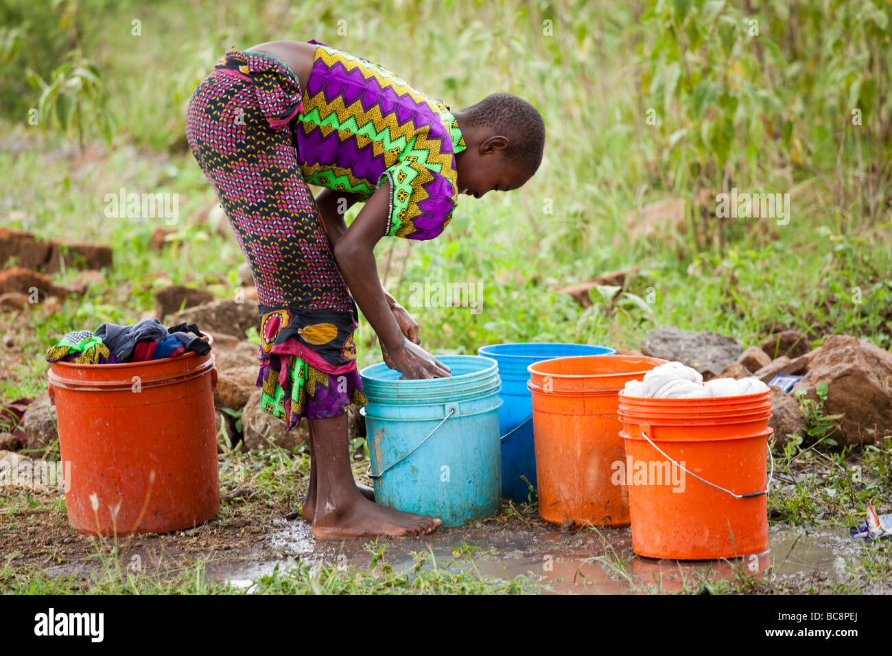 African girl washing laundry by hand in brightly coloured buckets ...