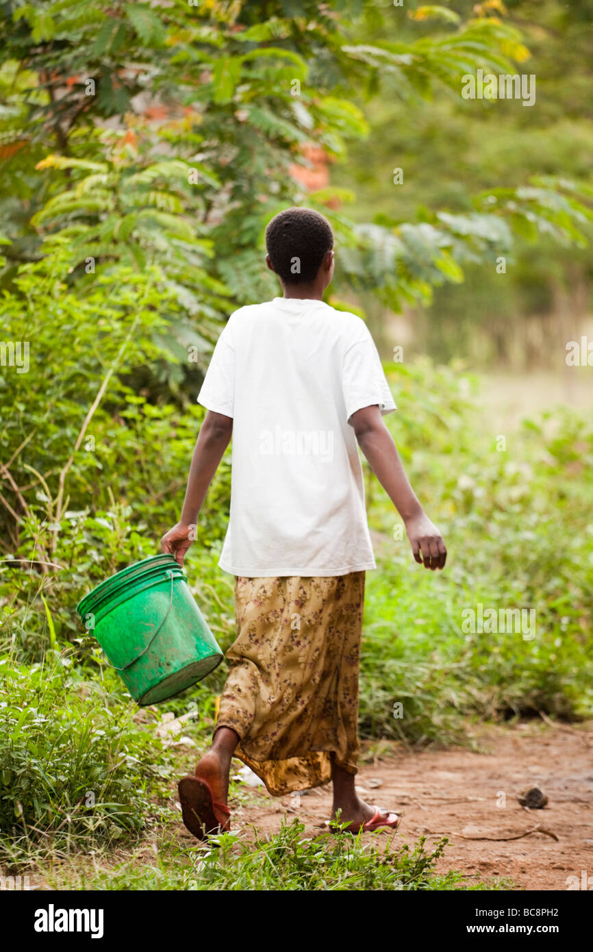 African girl walking to collect water with a bright green bucket. Kikwe