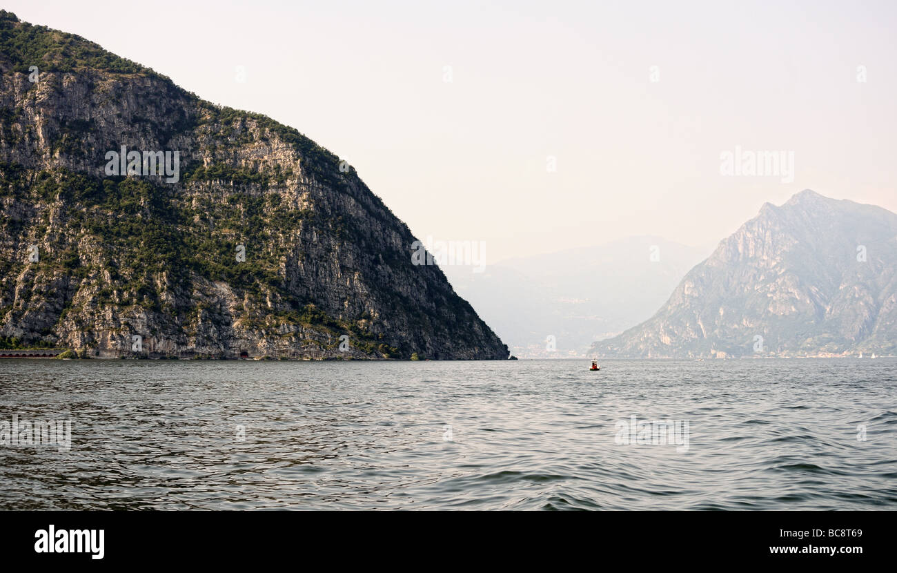 View over Lake Iseo towards a limestone rock formation with Monte Isola in the hazy background Stock Photo