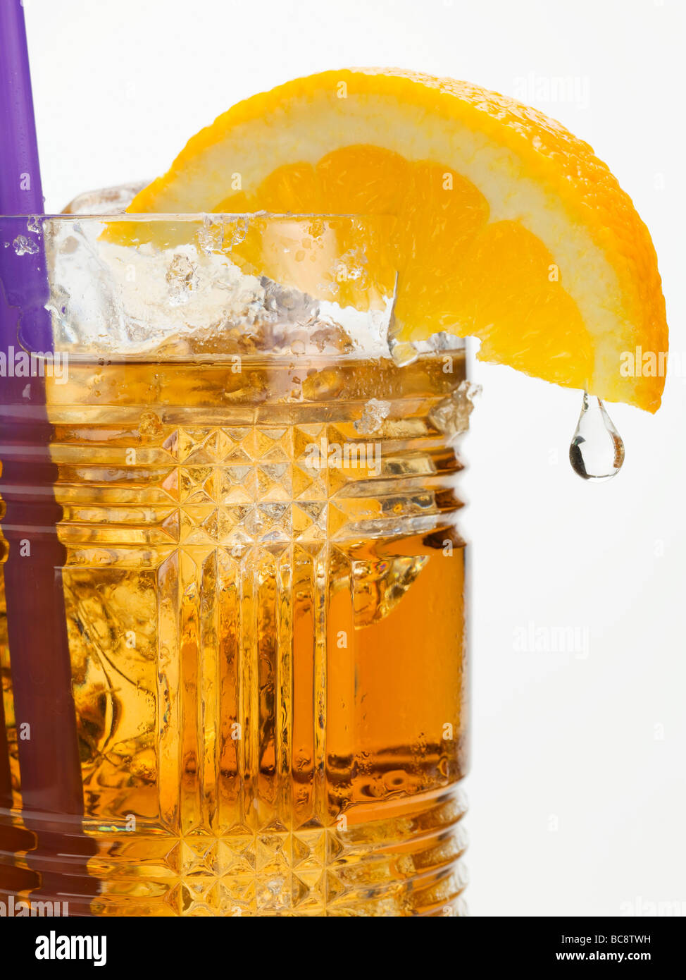 Rum drink with ice cubes and orange wedge with drip - Stock Photo