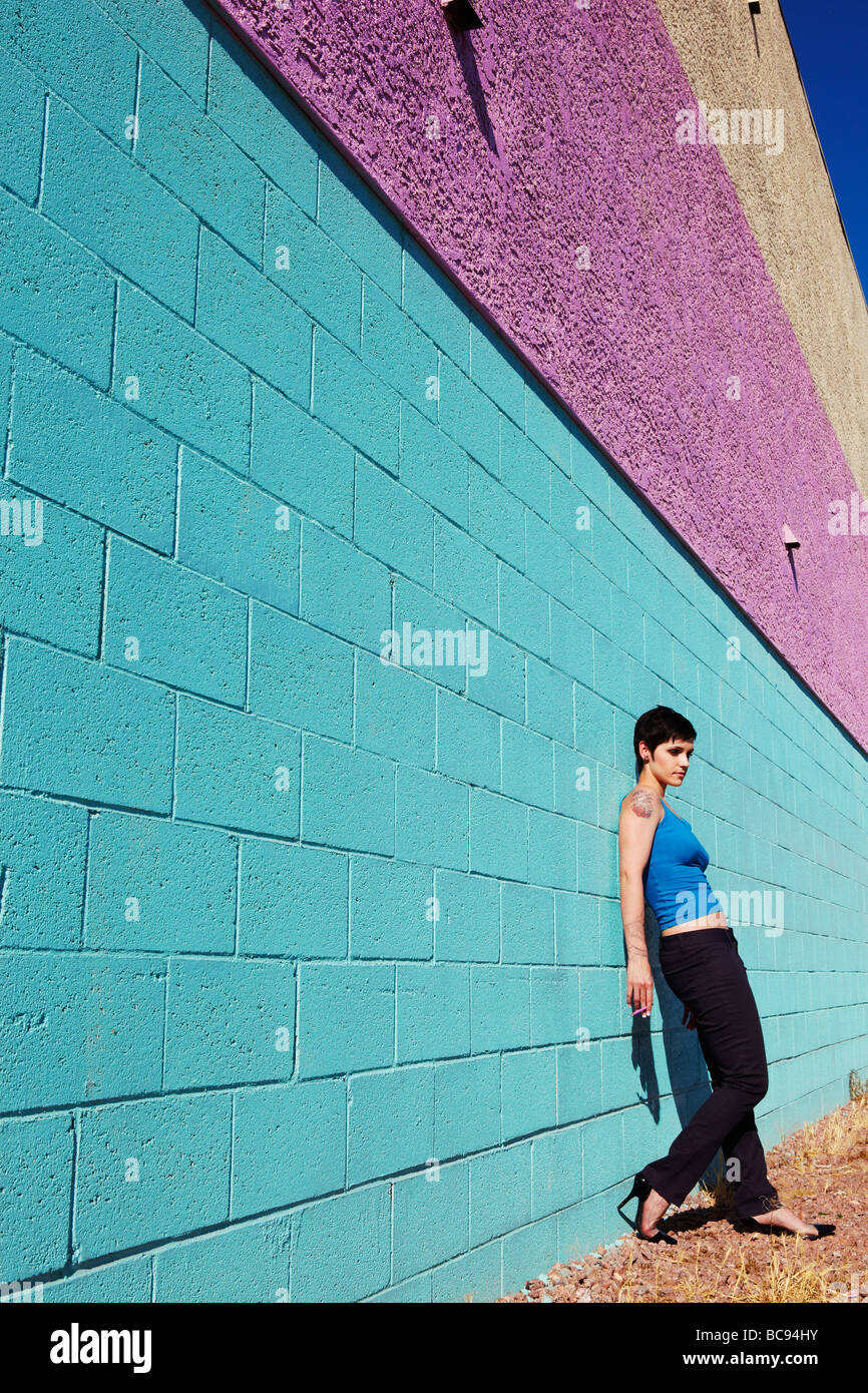 young woman leaning against a colourful wall, wide view Stock Photo