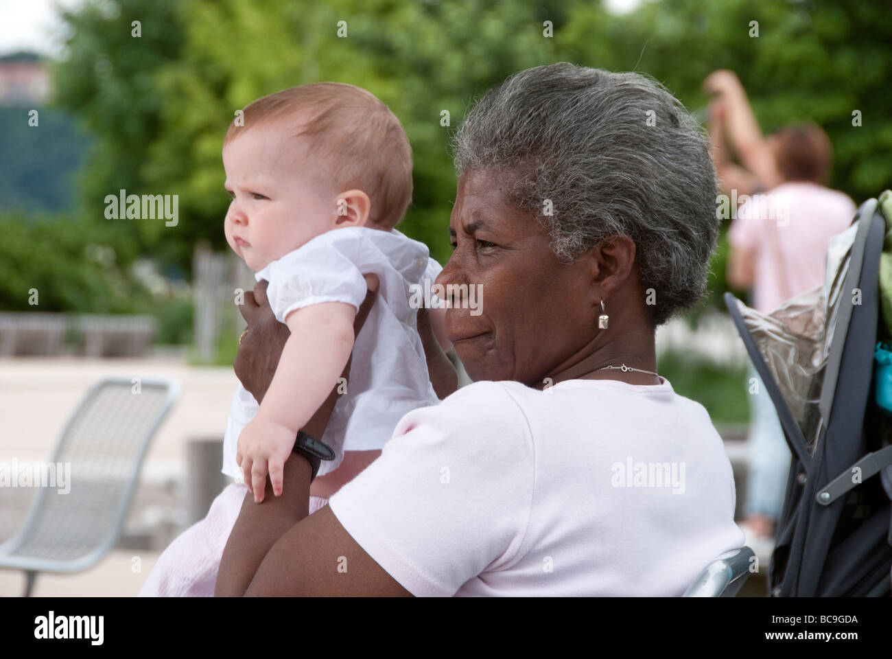black nursemaid nanny holding white baby infant in a New York City park Stock Photo