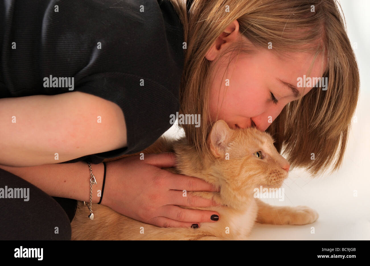 Beautiful blond blonde haired teen girl kissing marmalade kitty cat ginger tom cat orange tabby on white background MR PR Stock Photo
