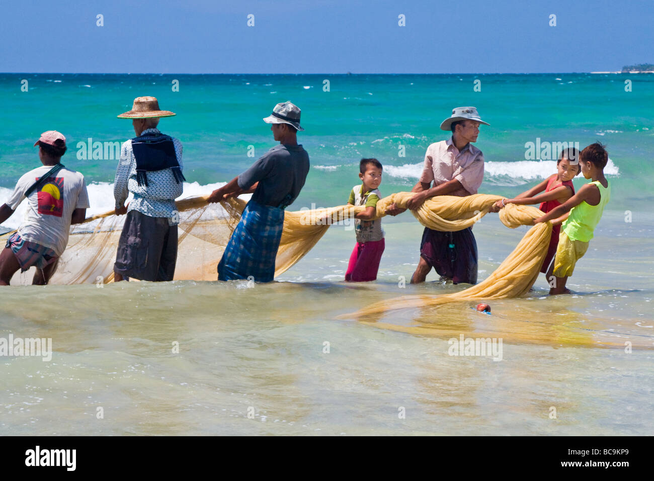 Fishermen pulling their net to land on the beach of Ngwe Saung, Myanmar with the help of local families Stock Photo