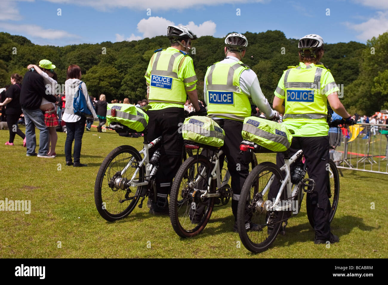 Three policemen on bikes watch the crowd at gay pride in Sheffield while a couple kiss Stock Photo
