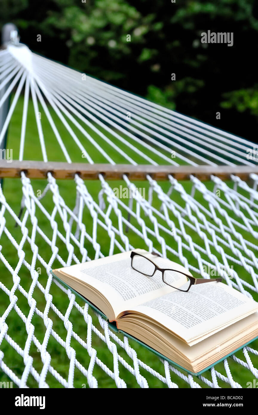 Summer reading staycation home vacation retirement weekend concept glasses eyeglasses spectacles open book backyard hammock. Stock Photo