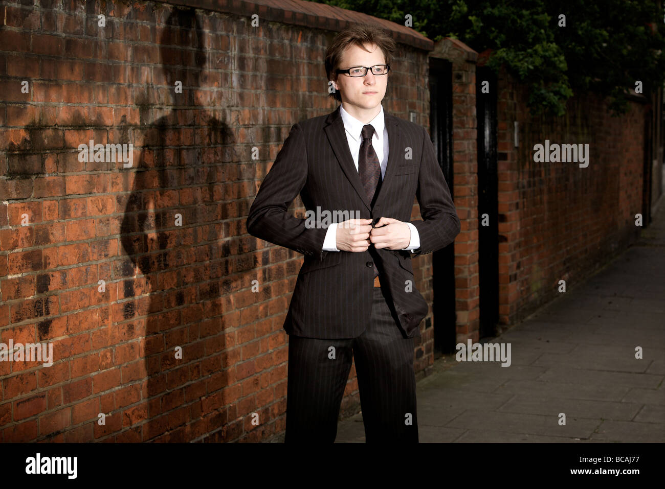 A suited young professional man stands on an urban street while buttoning his suit jacket in Marylebone, London, England. Stock Photo