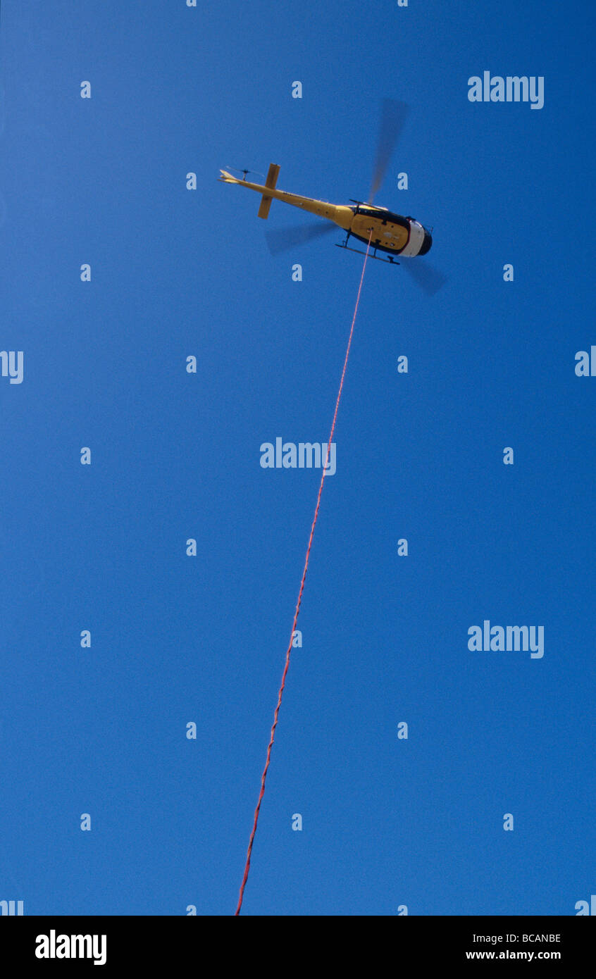 A massive cable extends from a Helicopter to transport equipment. Stock Photo