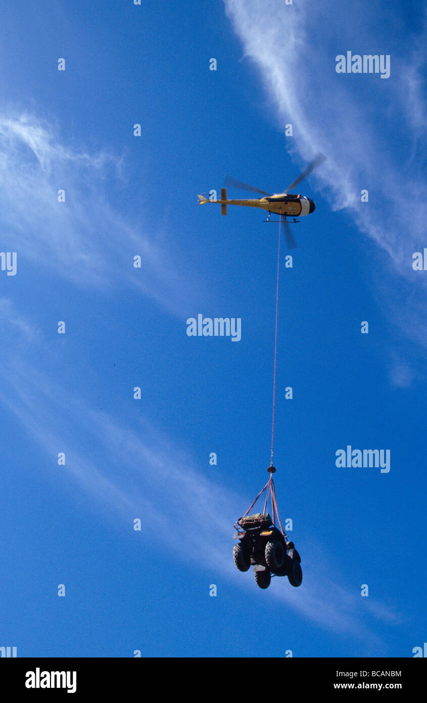 A cable extends from a Helicopter to transport an expedition vehicle. Stock Photo