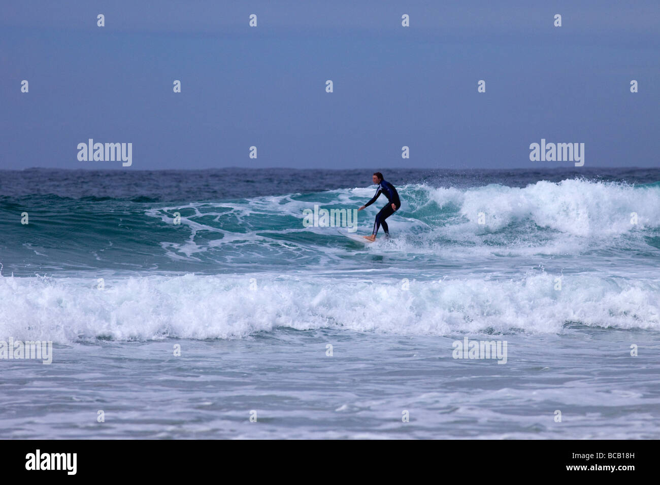 Surfing waves off Porthmeor beach in summer sun St Ives Cornwall