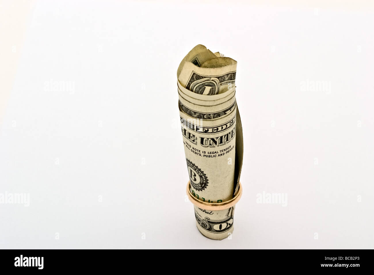 Roll of dollar bills with a gold wedding ring at the bottom Stock Photo