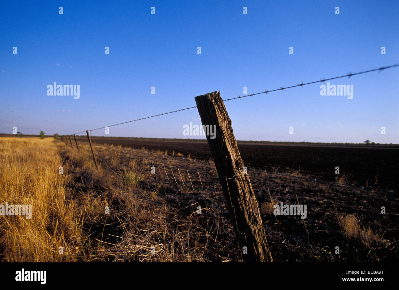 Farm fields and a crooked fence post and barbed wire fence at sunset