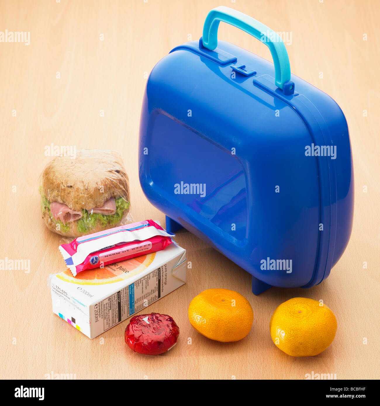 A children's school healthy lunch box / packed lunch with wholemeal roll, satsumas fruit, light cheese, orange juice and a sweet biscuit. Stock Photo