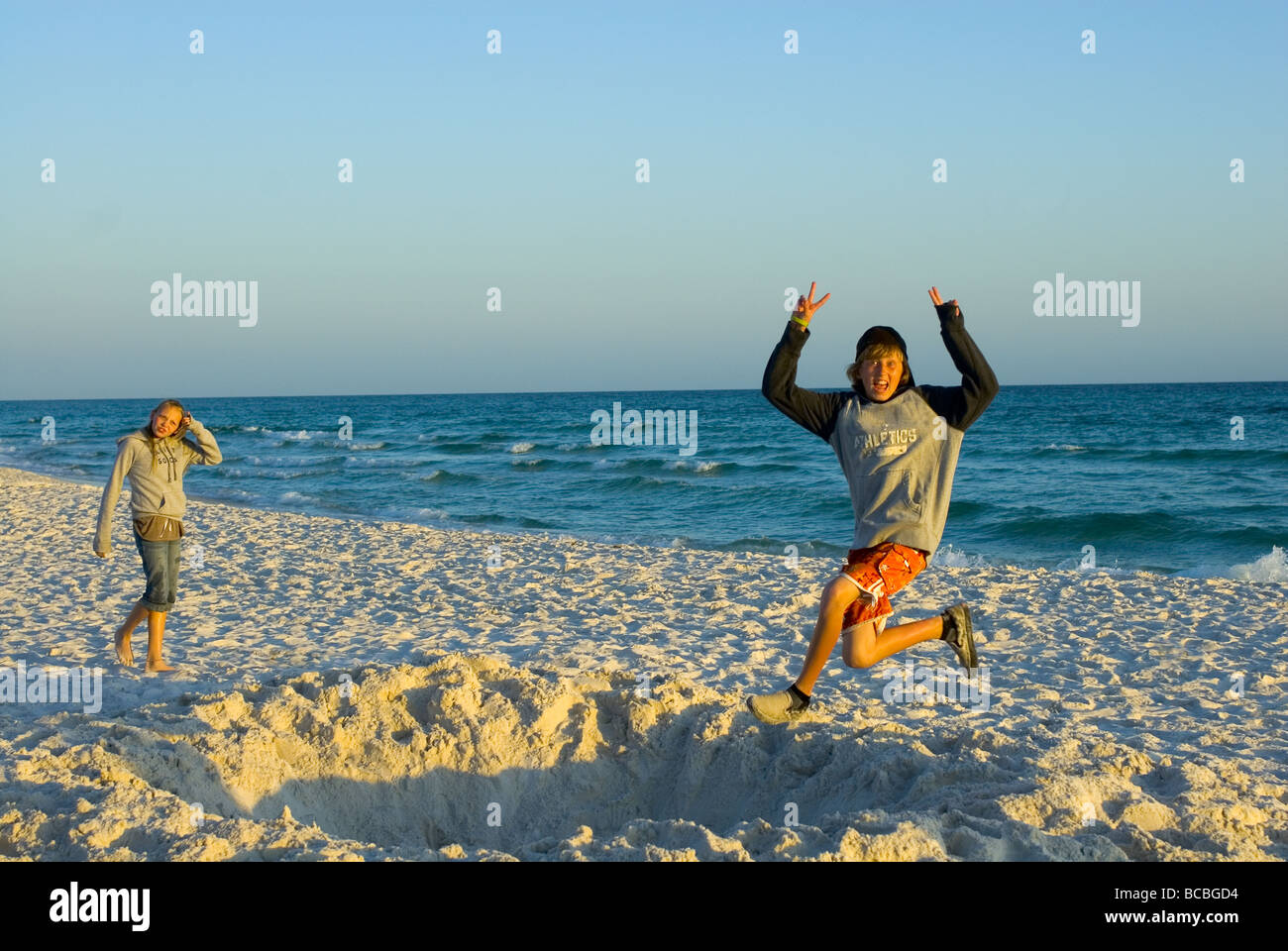 Young Boy Jumping into a Sand Pit at the Beach Signaling the Peace Sign