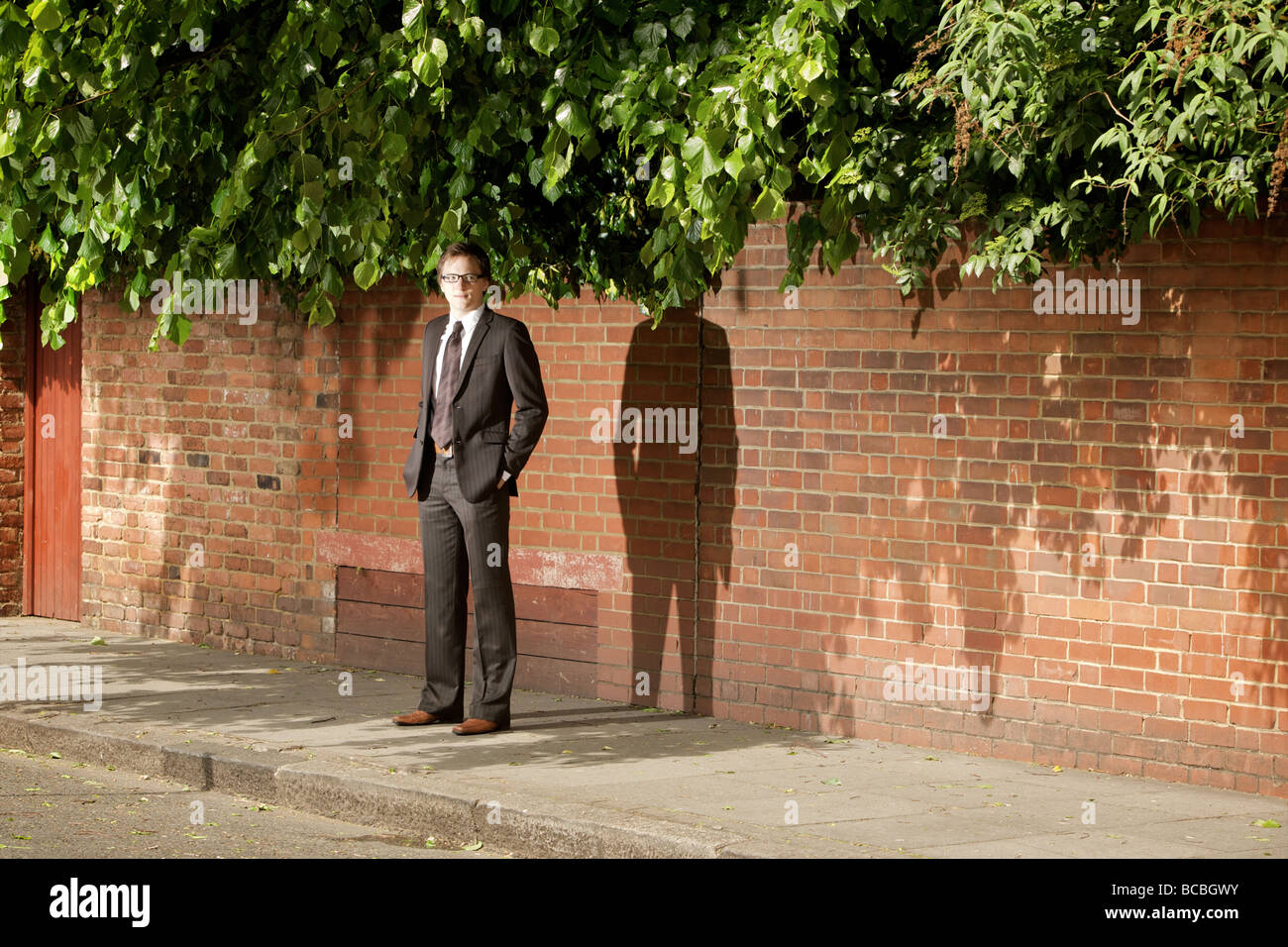 A suited young professional man stands waiting on an urban street  in the shade, Marylebone, London, England. Stock Photo