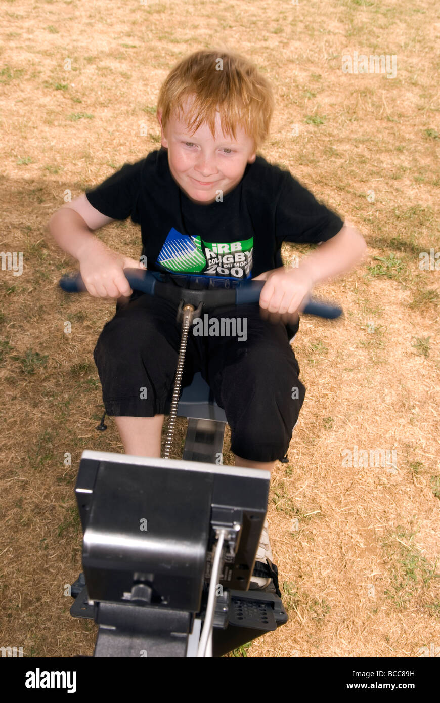 9 year old boy using rowing machine at a summer fayre, Wrecclesham, near Farnham, Surrey UK. Stock Photo