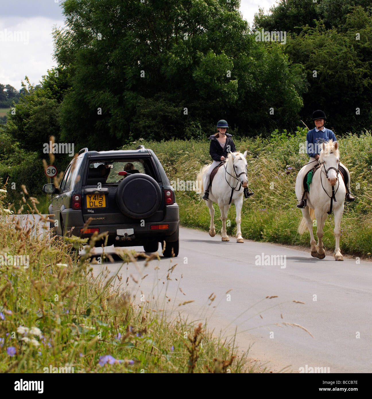 Horse riders pass a car on a country road in the Cotswolds Gloucestershire England UK Stock Photo