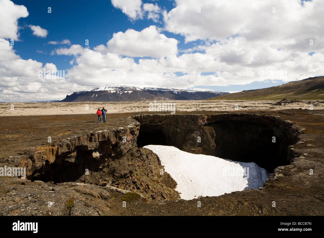 Mother and daughter standing next to a cave opening.  Surtshellir cave, Hallmundarhraun lava field, West Iceland. Stock Photo