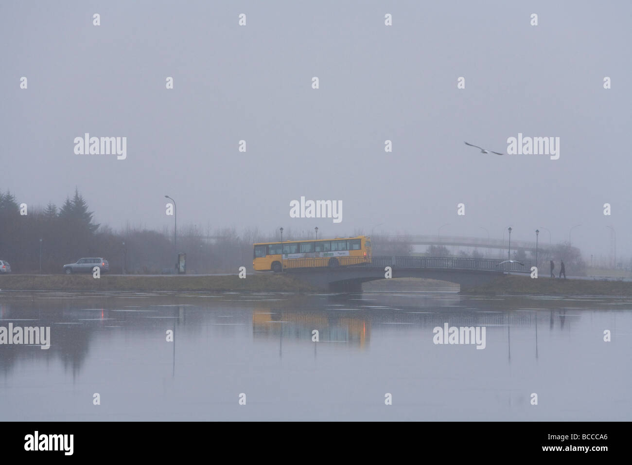 People crossing a bridge over Tjornin lake during a rainy foggy day Downtown Reykjavik Iceland Stock Photo