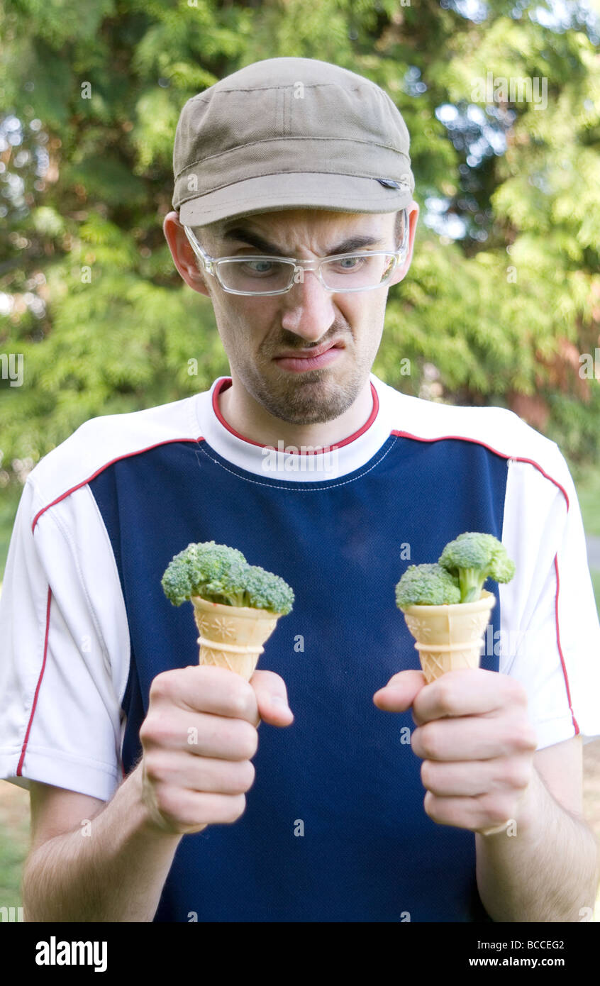 Young man frowning down at ice-cream cones filled with broccoli Stock Photo