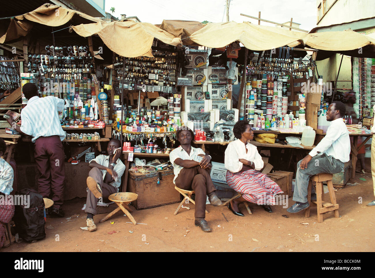 Traders sit relax waiting for customers at a market stall display of goods Kampala Uganda East Africa Stock Photo